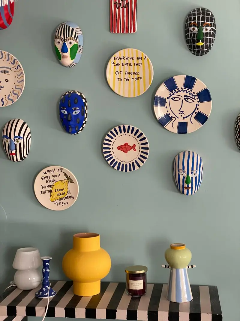 Mur de masques peints et d'assiettes à slogans au-dessus d'une console rayée